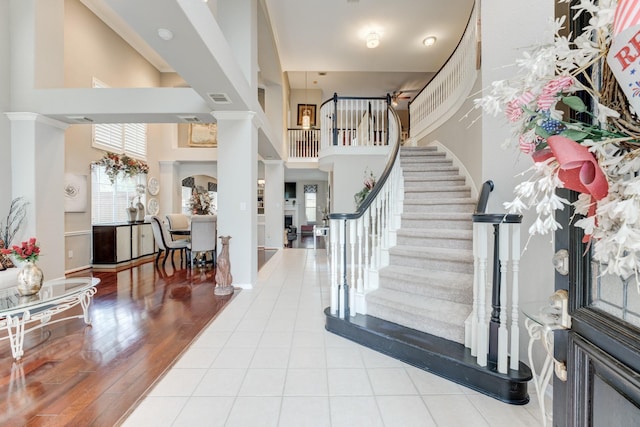 foyer entrance featuring ornate columns, plenty of natural light, a towering ceiling, and light wood-type flooring