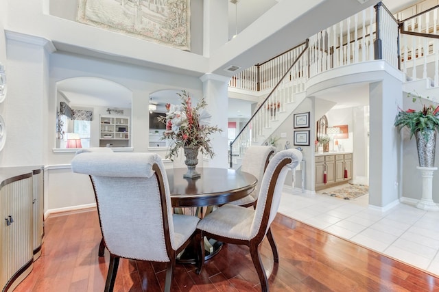 dining room with built in features, a towering ceiling, and wood-type flooring