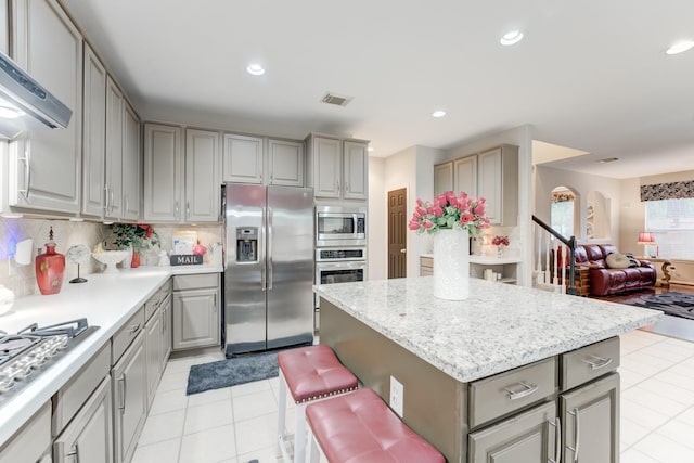 kitchen with appliances with stainless steel finishes, backsplash, gray cabinets, a center island, and a breakfast bar area