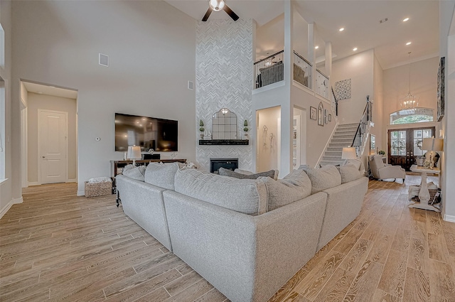 living room featuring a fireplace, ceiling fan with notable chandelier, light wood-type flooring, and a high ceiling