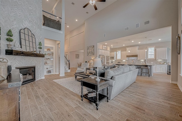 living room with a fireplace, light hardwood / wood-style floors, built in features, and a high ceiling