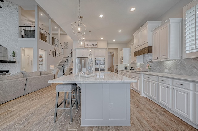 kitchen with stainless steel appliances, white cabinetry, a center island with sink, and light hardwood / wood-style flooring