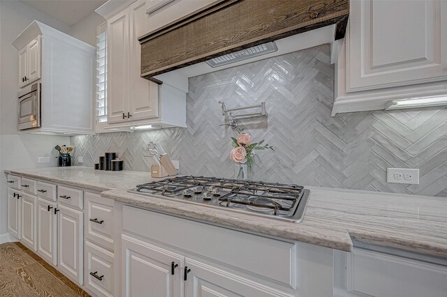 kitchen with light stone counters, stainless steel appliances, light hardwood / wood-style flooring, and white cabinets