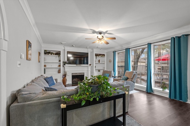 living room featuring dark hardwood / wood-style floors, crown molding, ceiling fan, a premium fireplace, and built in shelves