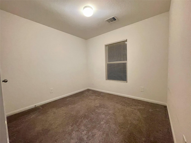 spare room with a textured ceiling and dark colored carpet