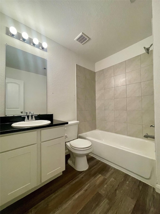 full bathroom with a textured ceiling, tiled shower / bath combo, hardwood / wood-style floors, vanity, and toilet