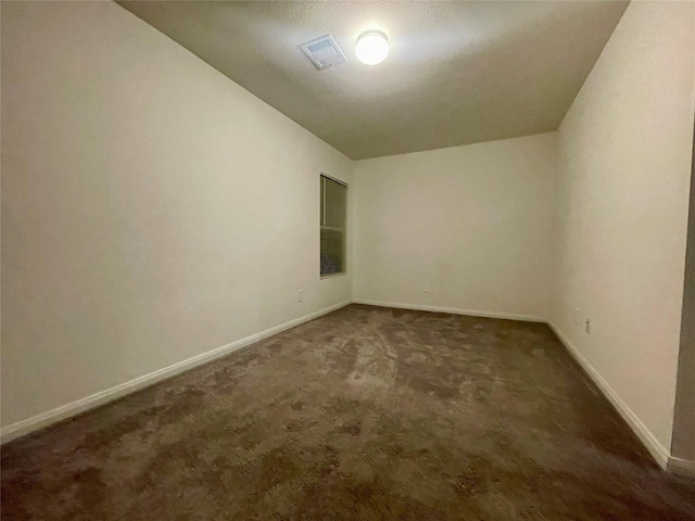 spare room featuring dark colored carpet and a textured ceiling