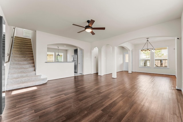 unfurnished living room featuring ceiling fan with notable chandelier and dark hardwood / wood-style floors