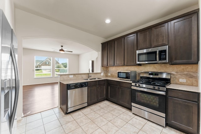 kitchen with kitchen peninsula, appliances with stainless steel finishes, sink, light tile patterned floors, and dark brown cabinetry