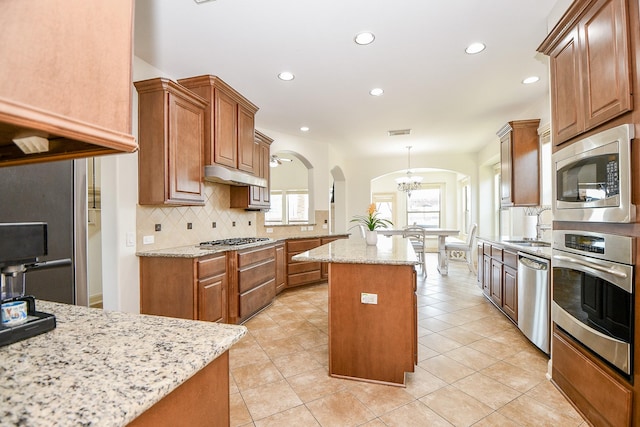 kitchen with light stone counters, tasteful backsplash, stainless steel appliances, and a center island