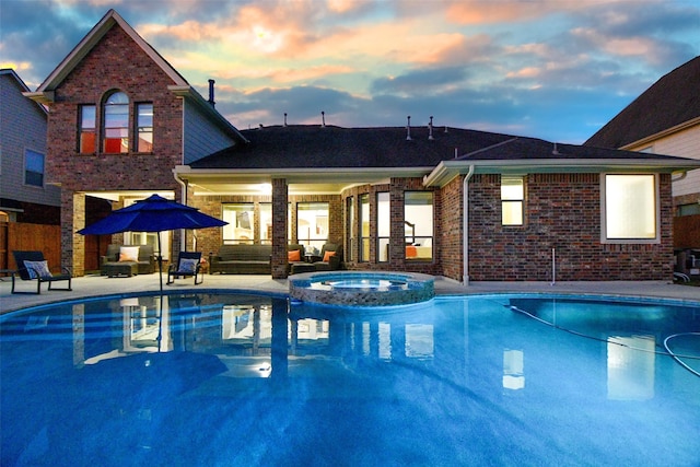 pool at dusk featuring an in ground hot tub and a patio