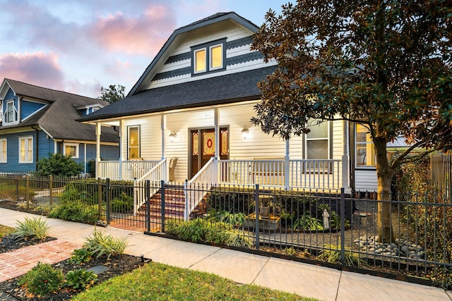 bungalow-style home featuring covered porch, a shingled roof, and a fenced front yard