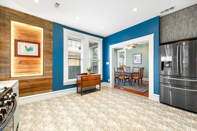 interior space featuring stainless steel fridge with ice dispenser, gas range oven, and wood walls