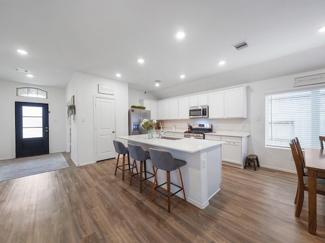 kitchen featuring appliances with stainless steel finishes, a kitchen bar, white cabinetry, dark hardwood / wood-style floors, and a kitchen island with sink