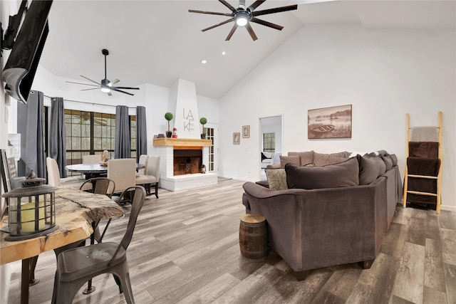 living room with ceiling fan, wood-type flooring, high vaulted ceiling, and a fireplace