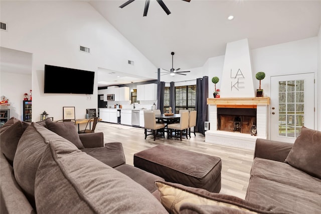 living room with ceiling fan, high vaulted ceiling, light hardwood / wood-style flooring, and a fireplace