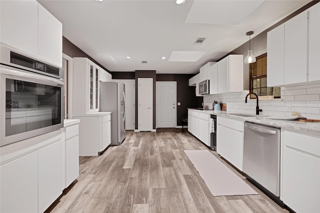 kitchen featuring white cabinets, sink, decorative light fixtures, light hardwood / wood-style flooring, and stainless steel appliances