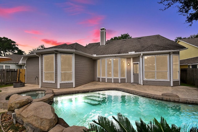 back house at dusk featuring a pool with hot tub and a patio