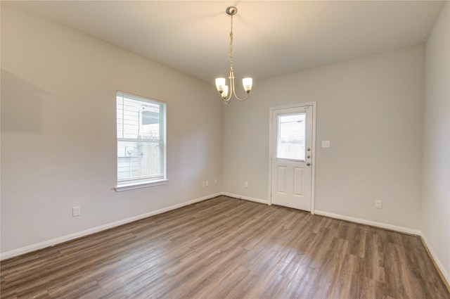 unfurnished room with an inviting chandelier and dark hardwood / wood-style flooring