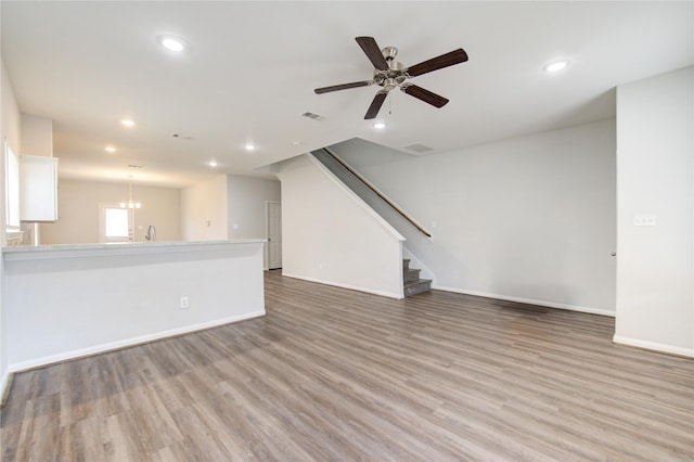 unfurnished living room featuring ceiling fan with notable chandelier and light hardwood / wood-style floors