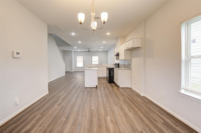 kitchen with wood-type flooring, decorative light fixtures, black / electric stove, white cabinets, and decorative backsplash