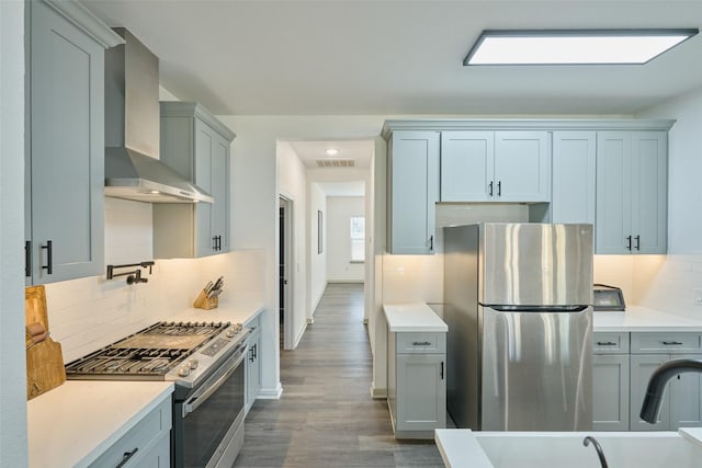 kitchen with wall chimney range hood, appliances with stainless steel finishes, dark hardwood / wood-style flooring, and tasteful backsplash