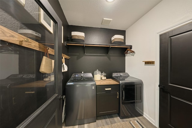 washroom featuring cabinets, a textured ceiling, light wood-type flooring, and washer and dryer