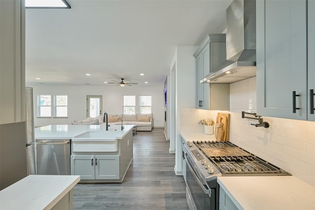 kitchen featuring tasteful backsplash, dark wood-type flooring, stainless steel appliances, wall chimney range hood, and sink