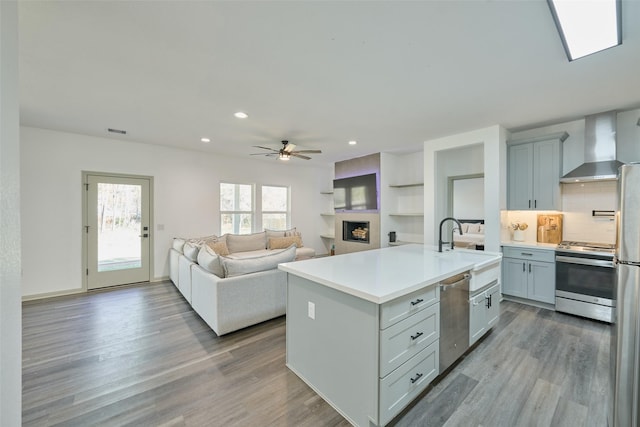 kitchen featuring appliances with stainless steel finishes, sink, backsplash, a kitchen island with sink, and wall chimney range hood