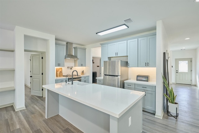 kitchen featuring stainless steel fridge, sink, wall chimney range hood, a large island with sink, and light hardwood / wood-style floors