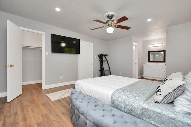 bedroom with ensuite bath, ceiling fan, a spacious closet, a closet, and light wood-type flooring