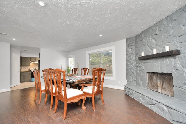 dining area featuring a stone fireplace, a textured ceiling, and dark hardwood / wood-style flooring