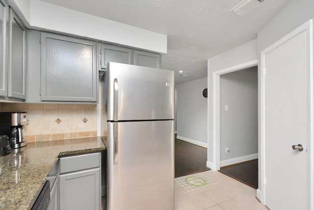 kitchen with tasteful backsplash, gray cabinetry, stainless steel fridge, and dark stone counters