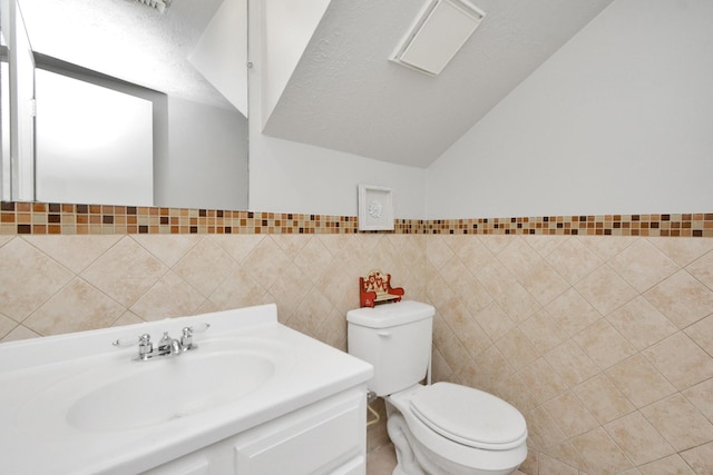 bathroom with lofted ceiling, tile walls, vanity, a textured ceiling, and toilet