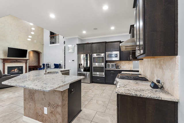 kitchen with sink, wall chimney exhaust hood, light stone countertops, a kitchen island with sink, and stainless steel appliances