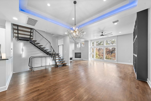 unfurnished living room featuring ceiling fan with notable chandelier, hardwood / wood-style floors, and a raised ceiling