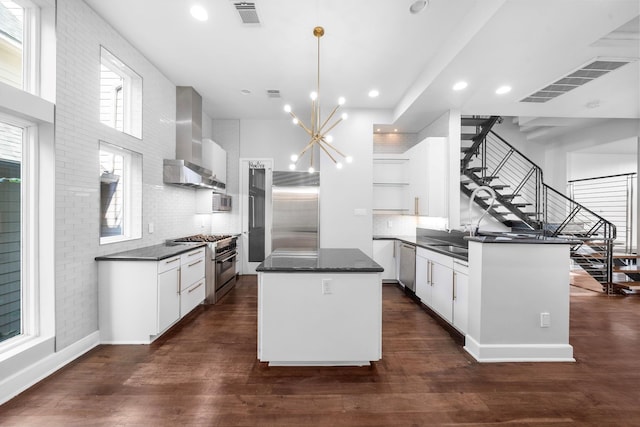 kitchen with a center island, white cabinetry, wall chimney range hood, decorative light fixtures, and high quality appliances