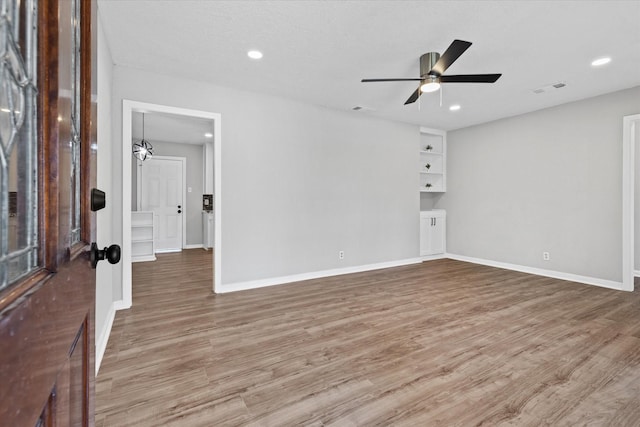 spare room featuring wood-type flooring, built in features, a textured ceiling, and ceiling fan