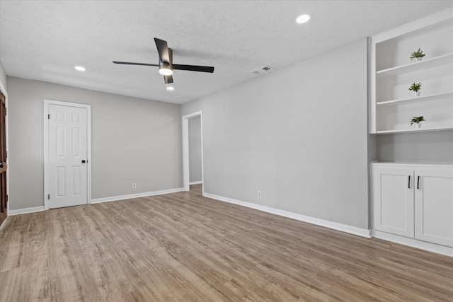 empty room with light hardwood / wood-style floors, built in shelves, a textured ceiling, and ceiling fan