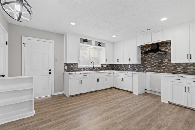 kitchen featuring a textured ceiling, white cabinets, wall chimney range hood, sink, and light hardwood / wood-style flooring