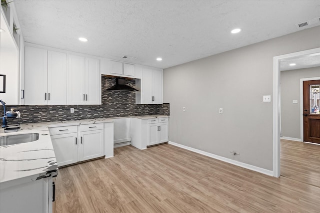 kitchen featuring wall chimney exhaust hood, sink, light wood-type flooring, white cabinetry, and a textured ceiling