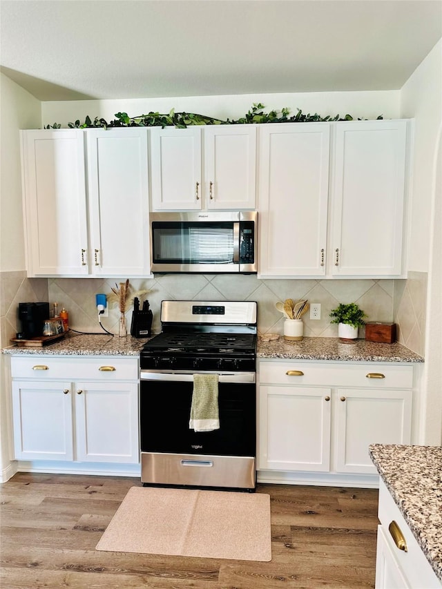 kitchen featuring light stone counters, white cabinetry, stainless steel appliances, and light wood-type flooring