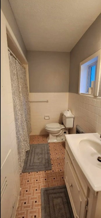 bathroom featuring vanity, toilet, tile walls, and a textured ceiling