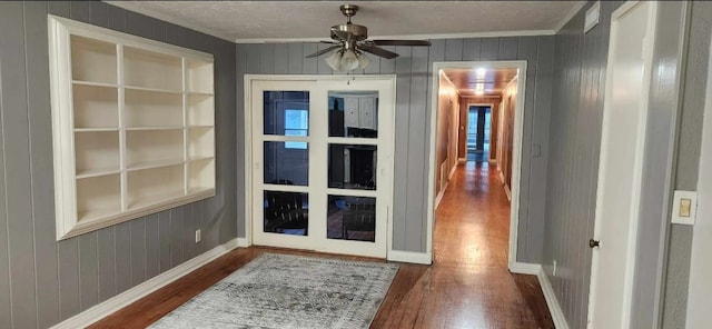 doorway to outside featuring crown molding, dark hardwood / wood-style flooring, built in features, ceiling fan, and wood walls