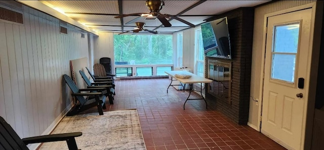 interior space featuring ceiling fan, a brick fireplace, and wood walls