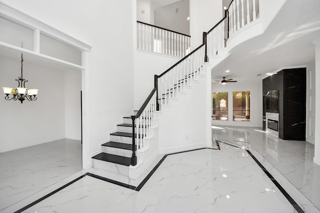 staircase featuring ceiling fan with notable chandelier and a high ceiling