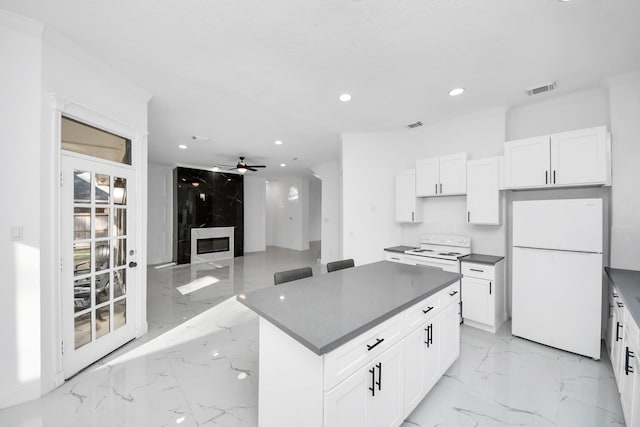 kitchen with white appliances, a kitchen island, ceiling fan, a premium fireplace, and white cabinets