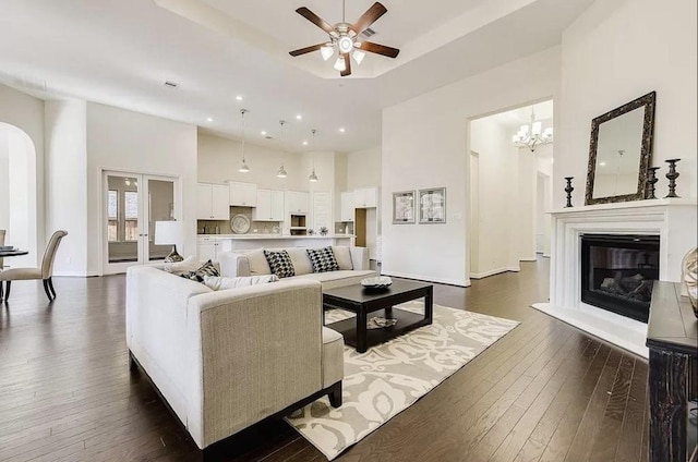 living room with a towering ceiling, french doors, ceiling fan with notable chandelier, and dark wood-type flooring