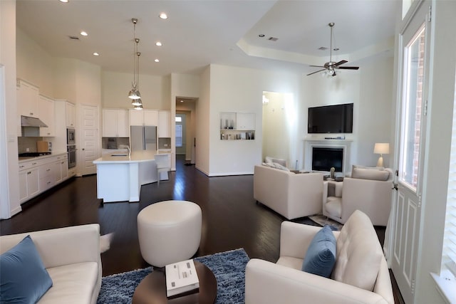 living room featuring ceiling fan, dark wood-type flooring, sink, and a towering ceiling