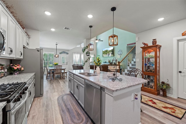 kitchen featuring appliances with stainless steel finishes, decorative light fixtures, light hardwood / wood-style floors, sink, and a kitchen island with sink